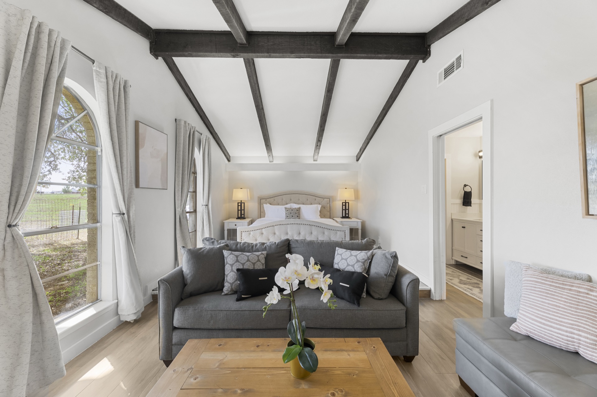 Master suite with king bed, sofa, exposed beams, and arched windows